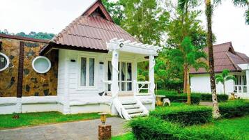 A white building with a brown roof, a porch, and a stone wall.
