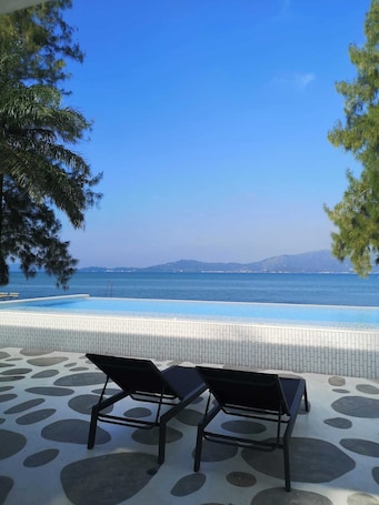 A poolside area with two lounge chairs facing a clear blue sea and distant mountains.