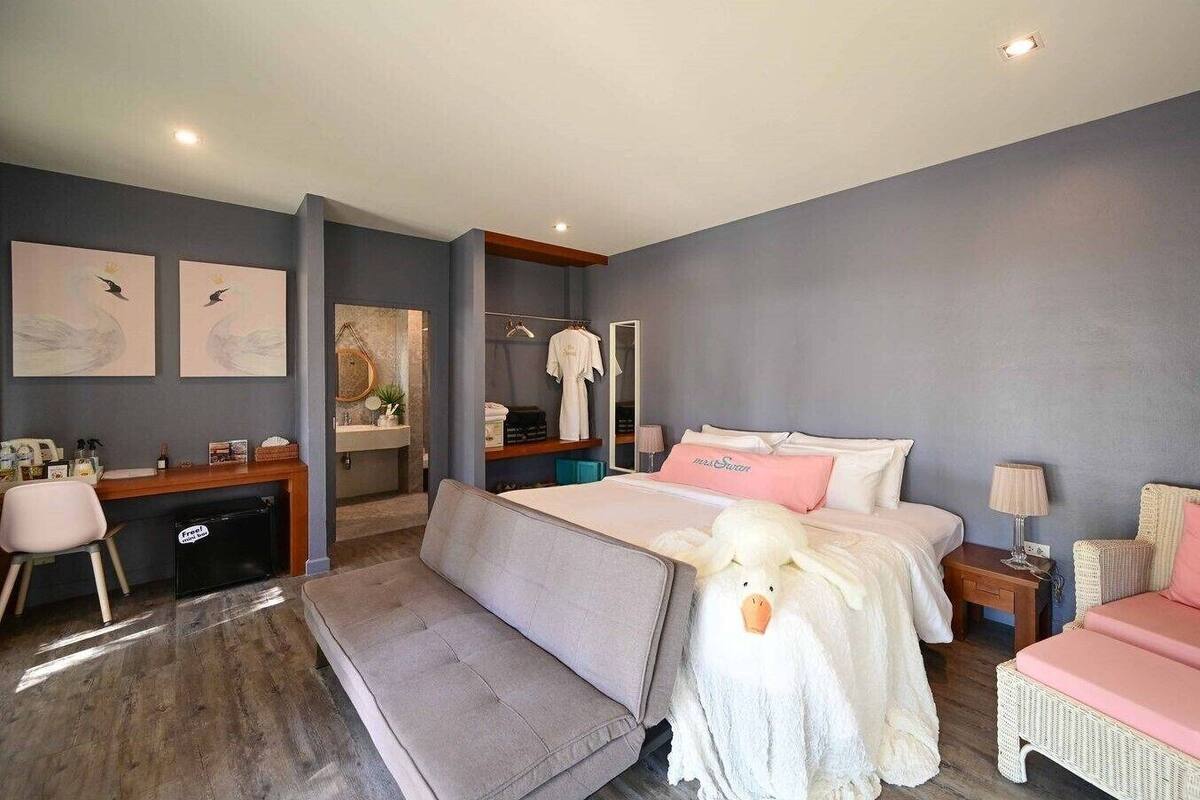 A modern hotel room with a bed, a desk, a chair, a sofa, and a small table.