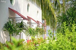 Un edificio blanco con toldo rojo, rodeado de abundante vegetación y palmeras.