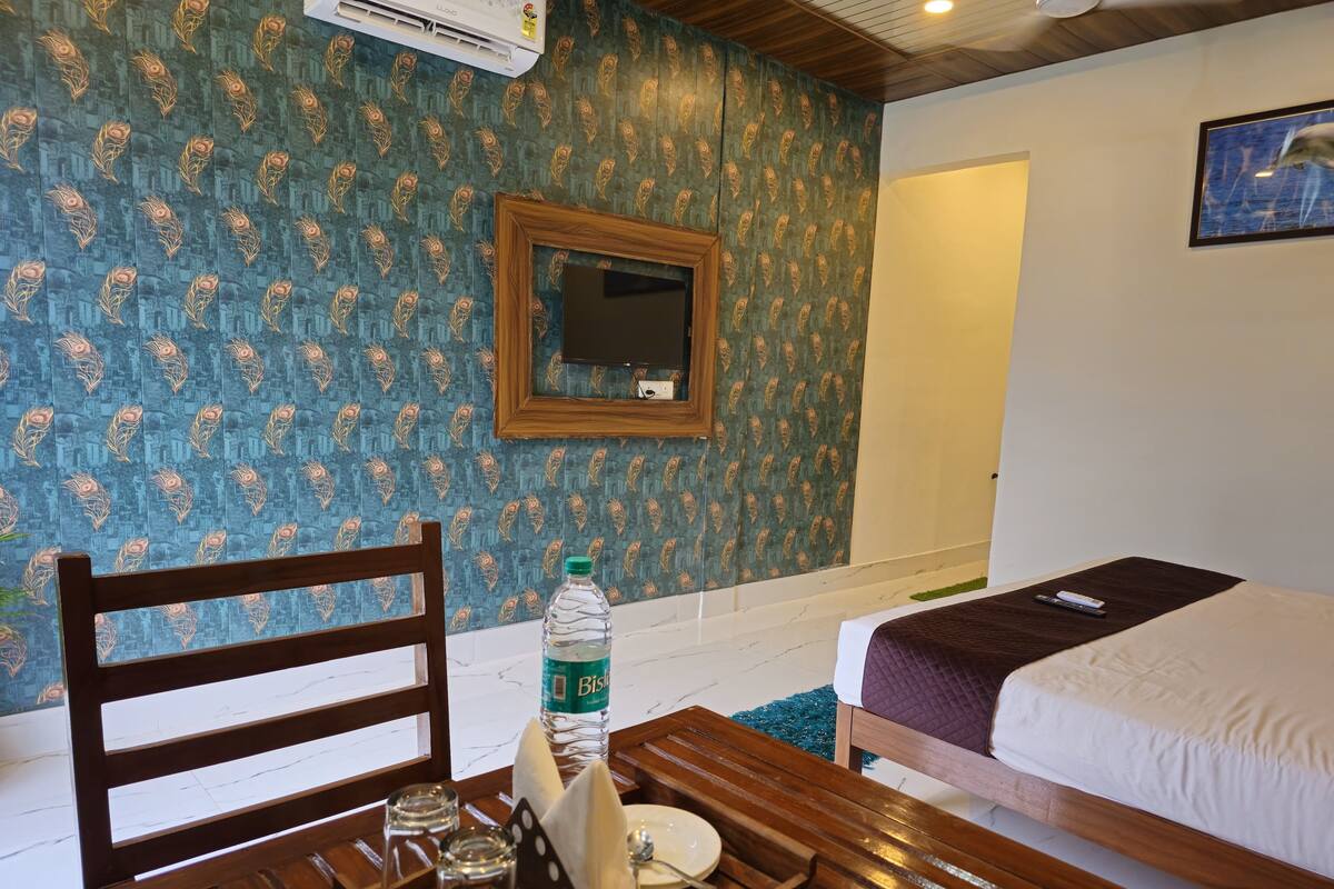 Una habitación con una cama, una mesa de madera con una botella y vasos, una silla, un espejo y una pared con diseño.