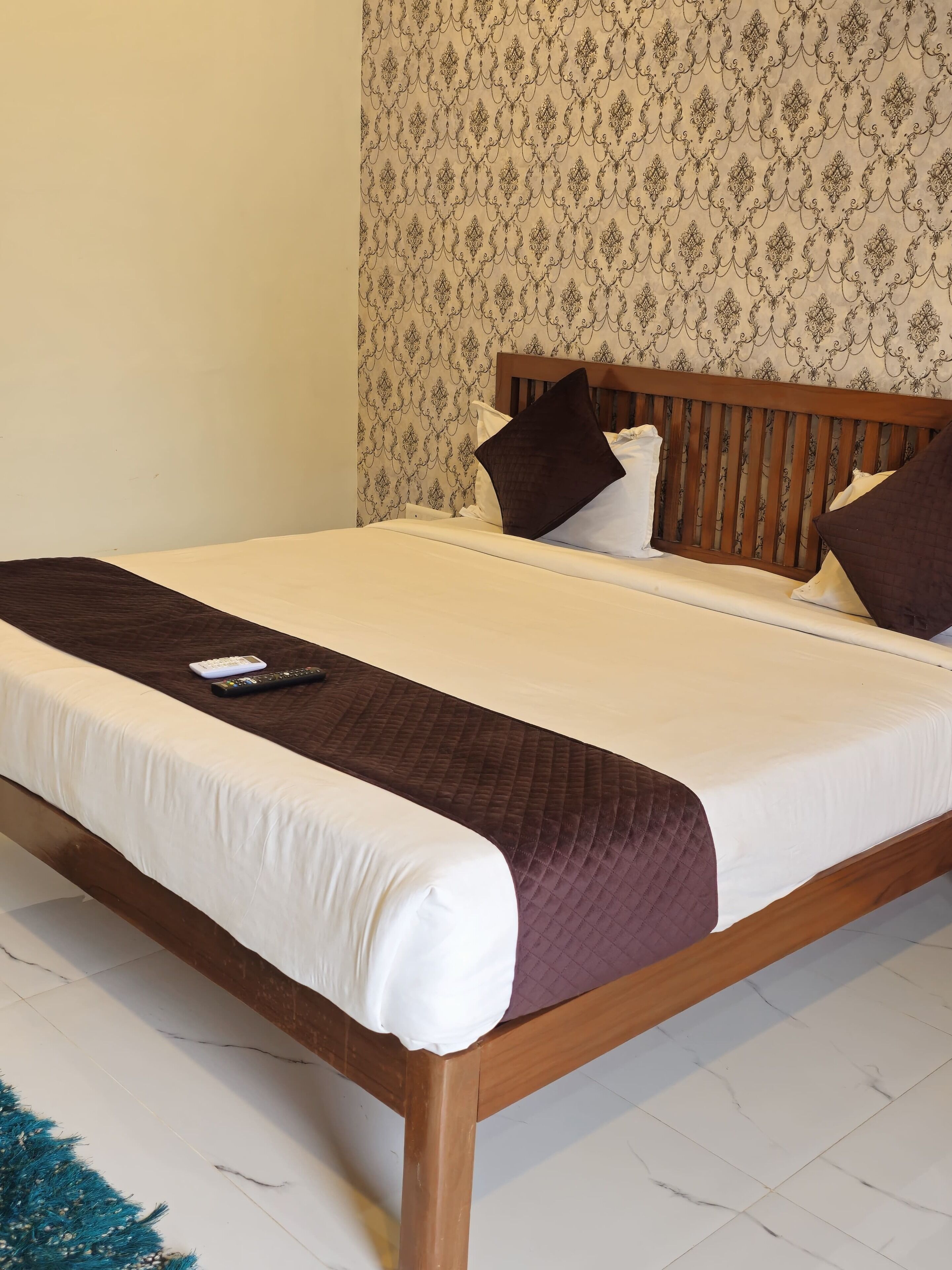 A neatly made bed with a wooden frame, white bedding, and a brown quilt.
