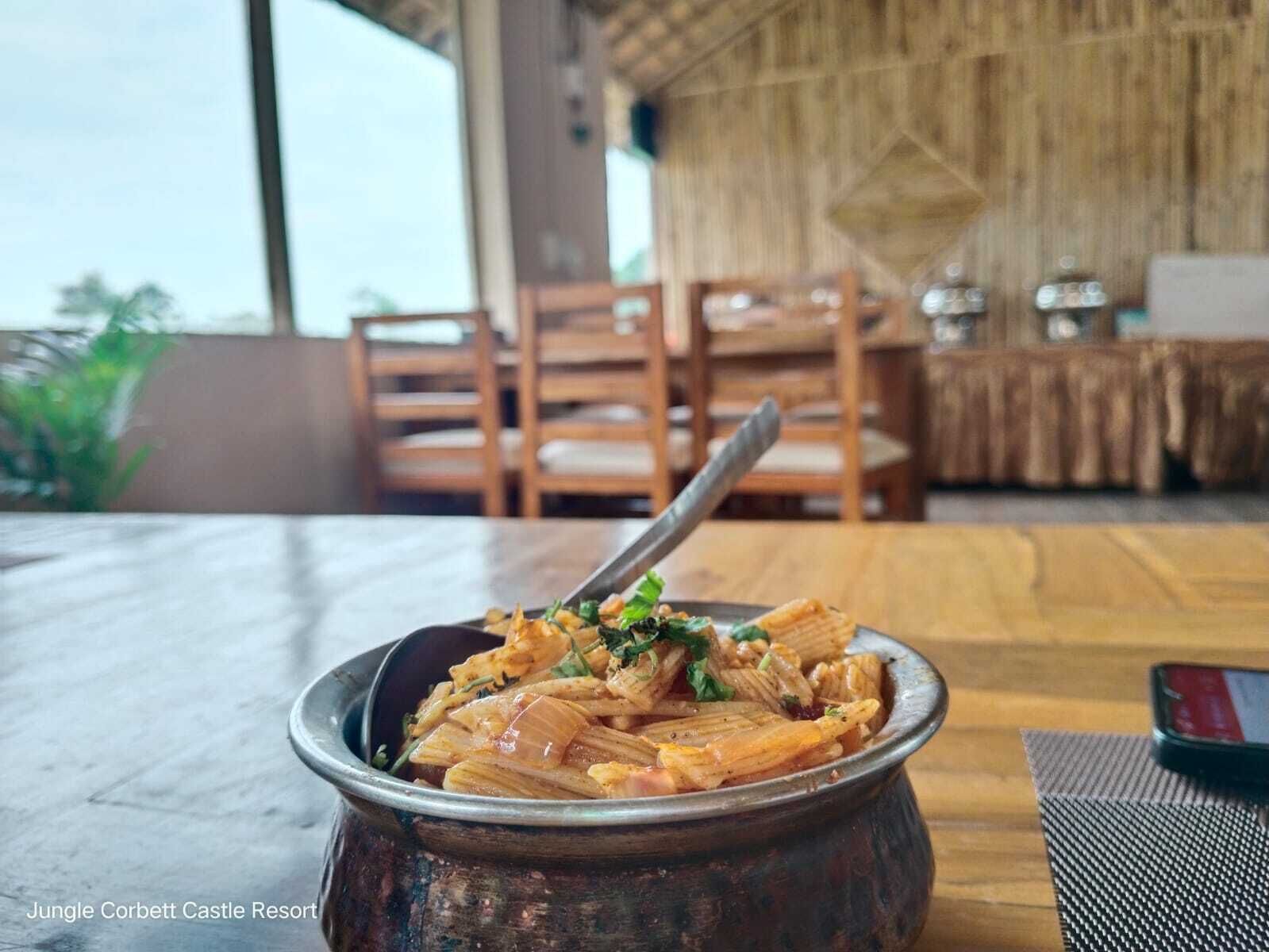 Un bol de pâtes avec une cuillère, posé sur une table en bois dans un restaurant.