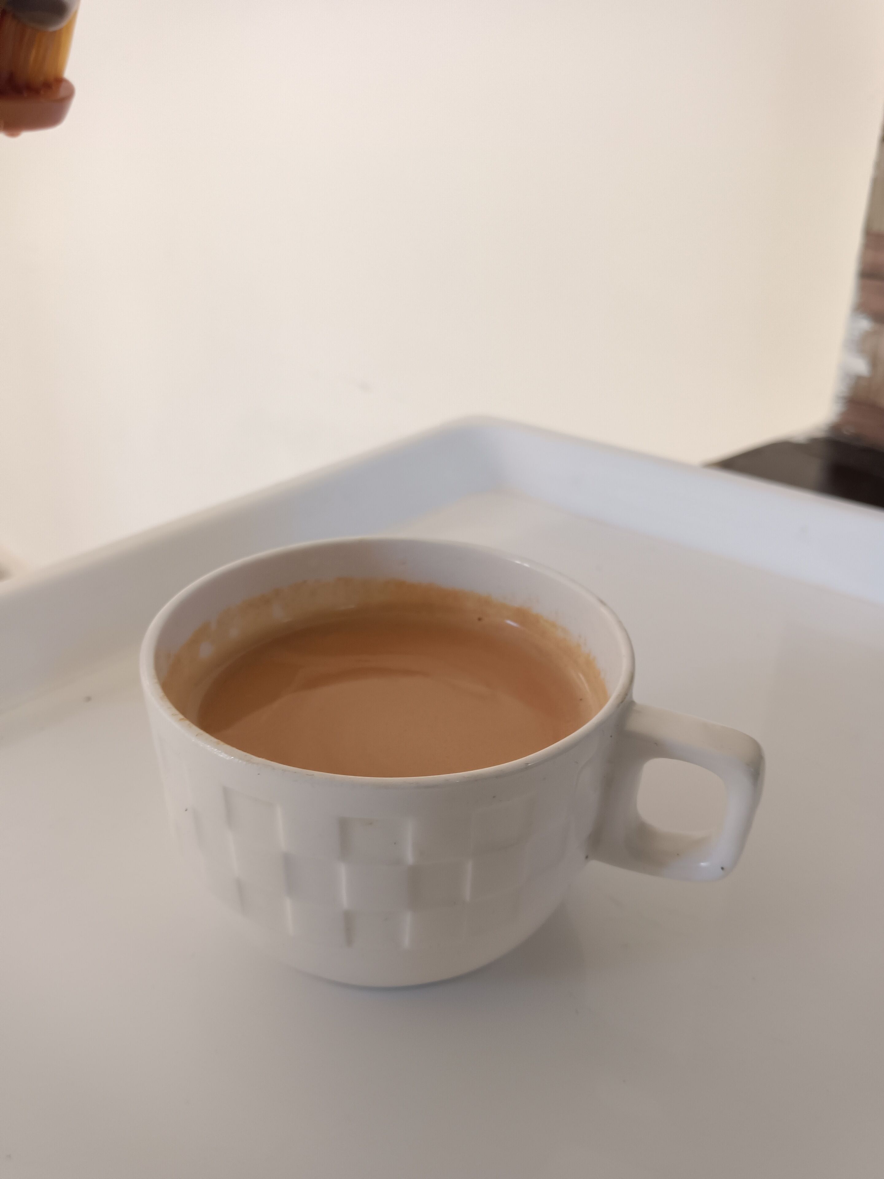 Una taza de cerámica blanca con asa, llena de un líquido marrón claro, sobre una bandeja blanca.