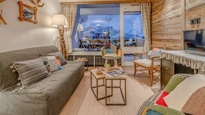 Ein gemütliches Wohnzimmer mit Sofa, Sessel und Couchtisch. Ein großes Fenster bietet Blick auf die Stadt.