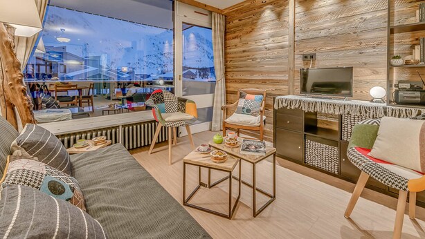 Ein modernes Wohnzimmer mit großem Fenster, einem gemütlichen Sofa, einem Couchtisch und einem Fernseher.