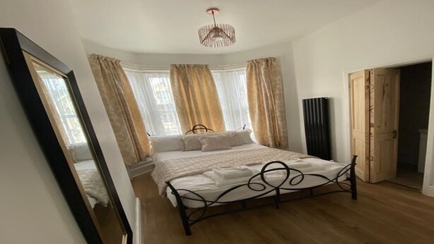 A bedroom with a bed, a mirror, a wardrobe, and a window with curtains. - Alexander Hotel (Blackpool)