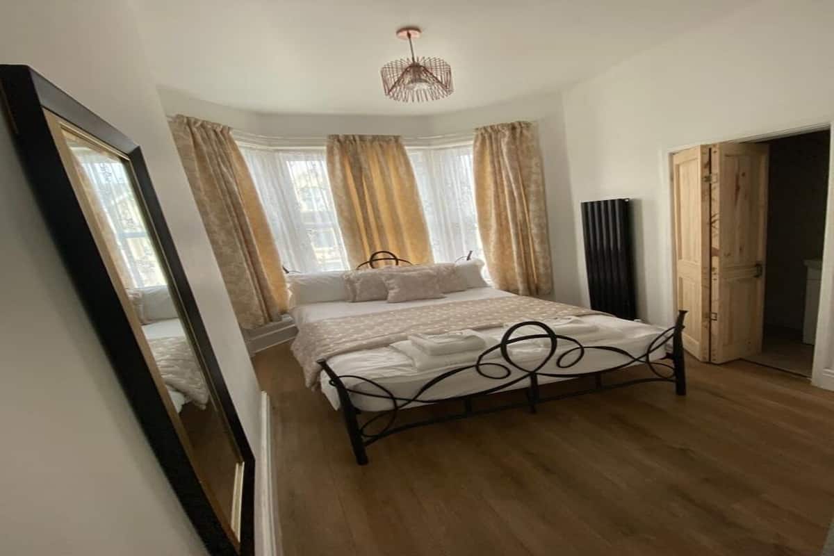 Um quarto com cama, espelho, guarda-roupa e janela com cortinas.