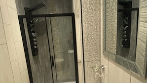 A modern bathroom with a glass-enclosed shower, a white sink with a black faucet, and a large mirror above the sink. - Alexander Hotel (Blackpool)