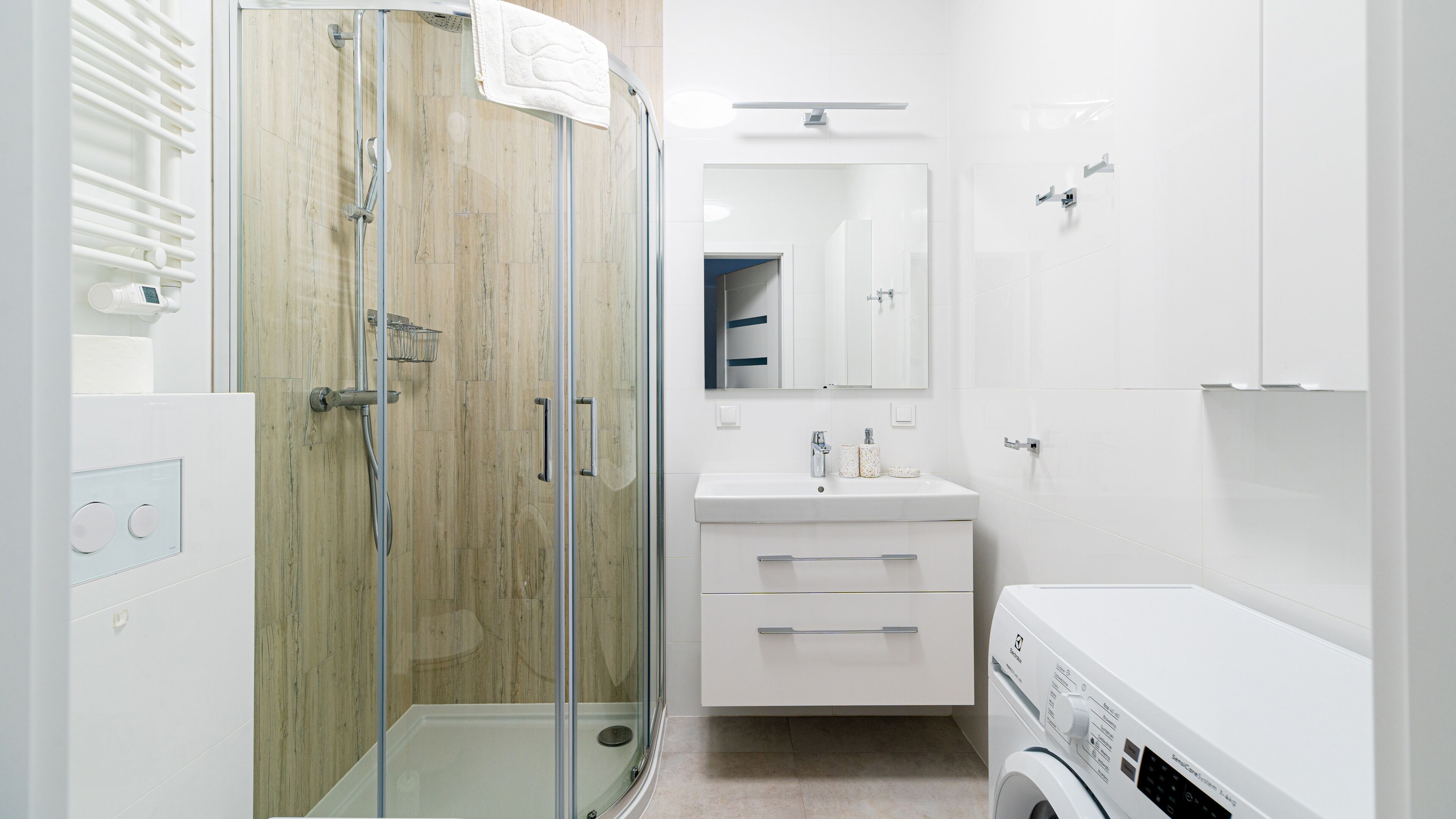 A modern bathroom with a glass-enclosed shower, a white sink with a mirror above, and a built-in washing machine.