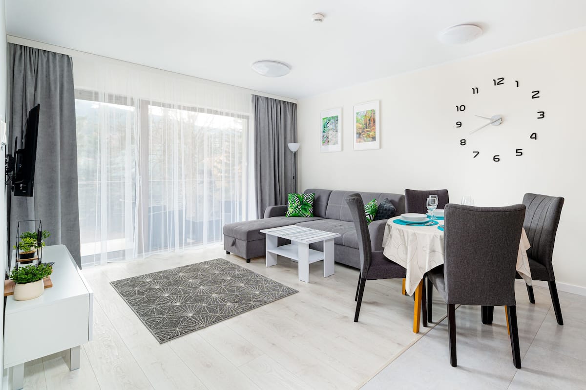 A modern living room with a sofa, dining table, chairs, a clock, and a TV.