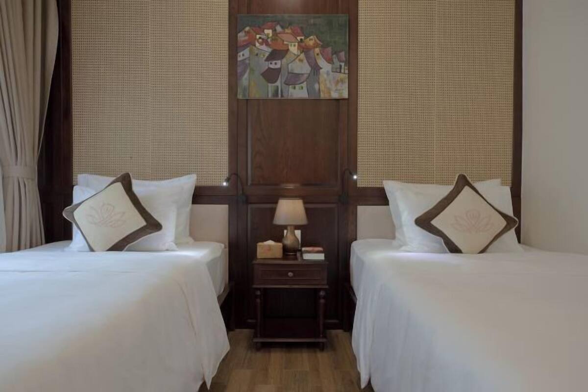 A hotel room with two beds, a nightstand with a lamp, and a painting on the wall.