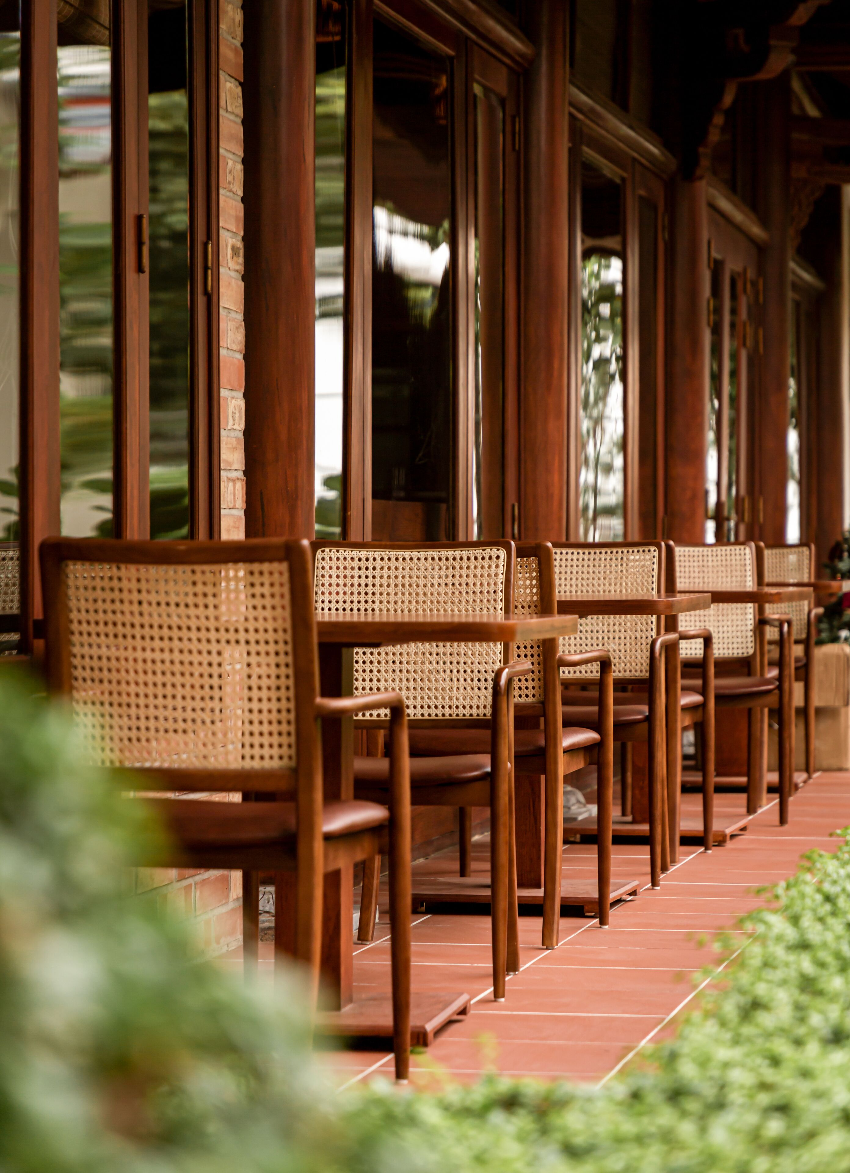 A row of wooden chairs with woven seats and backs, arranged on a tiled patio.