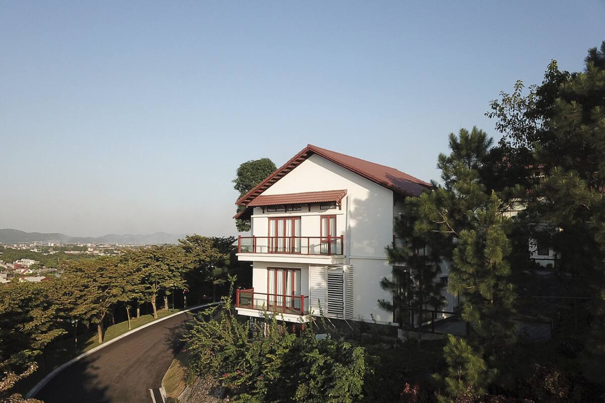 A two-story building with a red roof and white walls, surrounded by trees and a curved road.