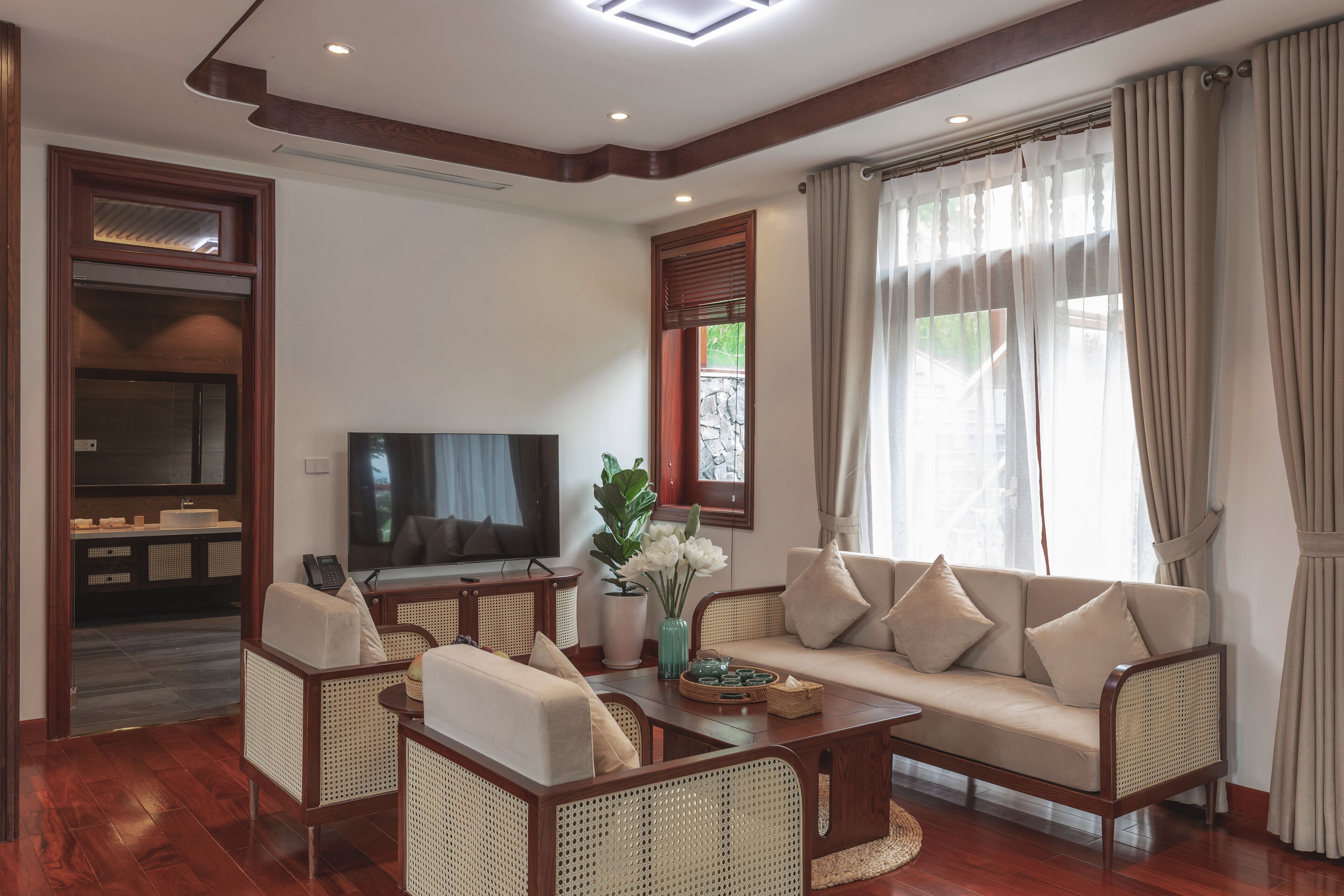 A living room with a sofa, chairs, a coffee table, a TV, and a window with curtains.