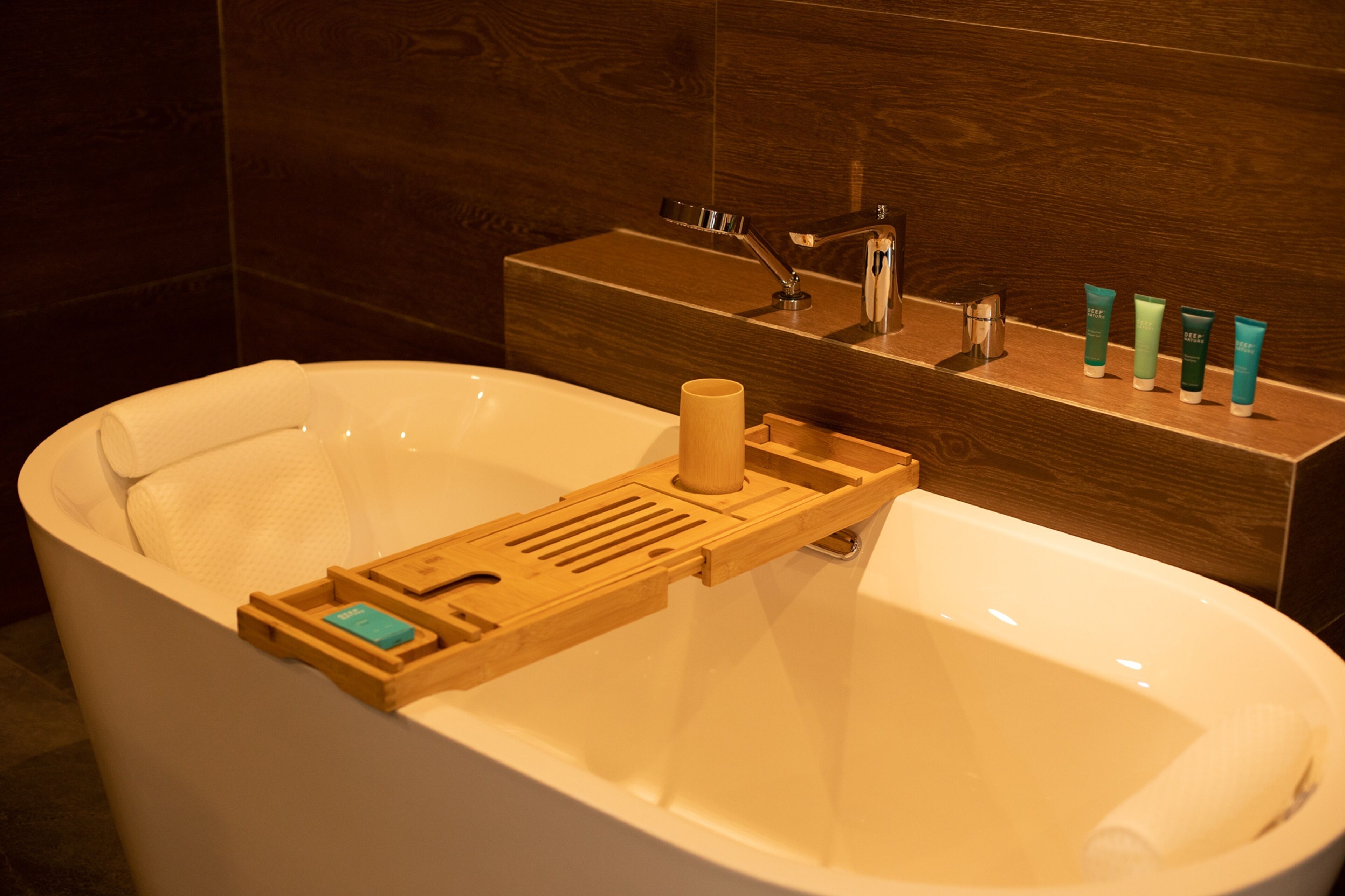 A modern bathroom with a bathtub, wooden tray, and toiletries.