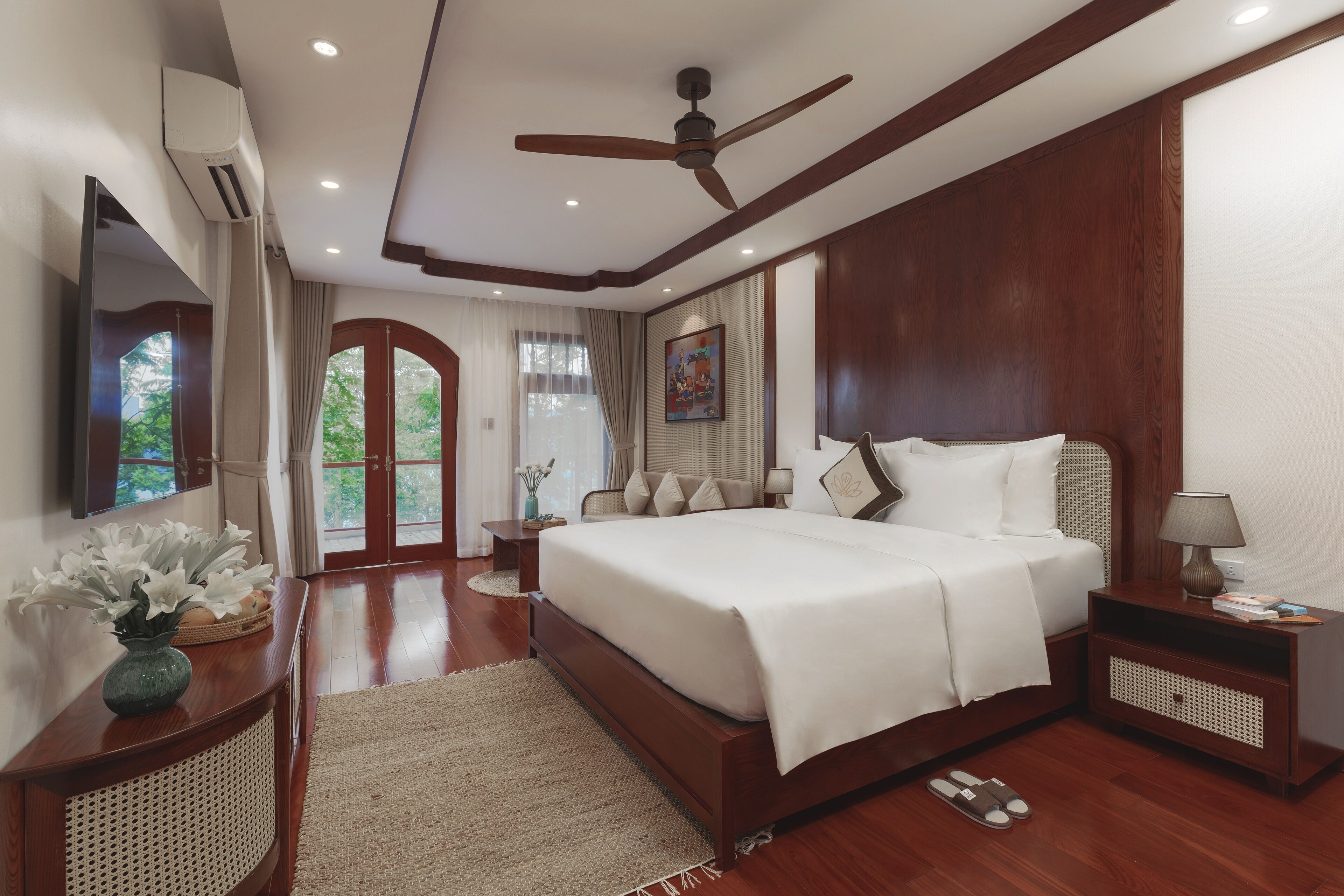 A spacious bedroom with a large bed, a ceiling fan, a TV, and a view of the outdoors.