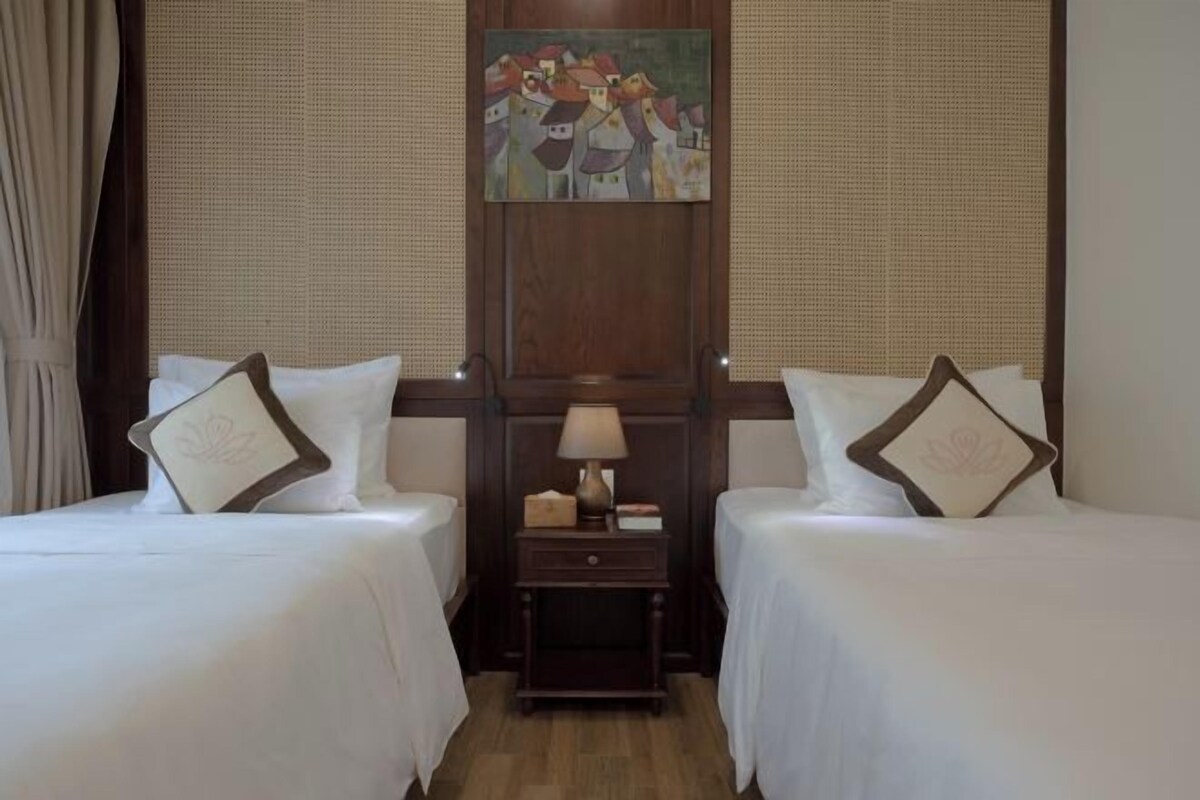 Una habitación de hotel con dos camas, una mesita de noche con lámpara y un cuadro en la pared.