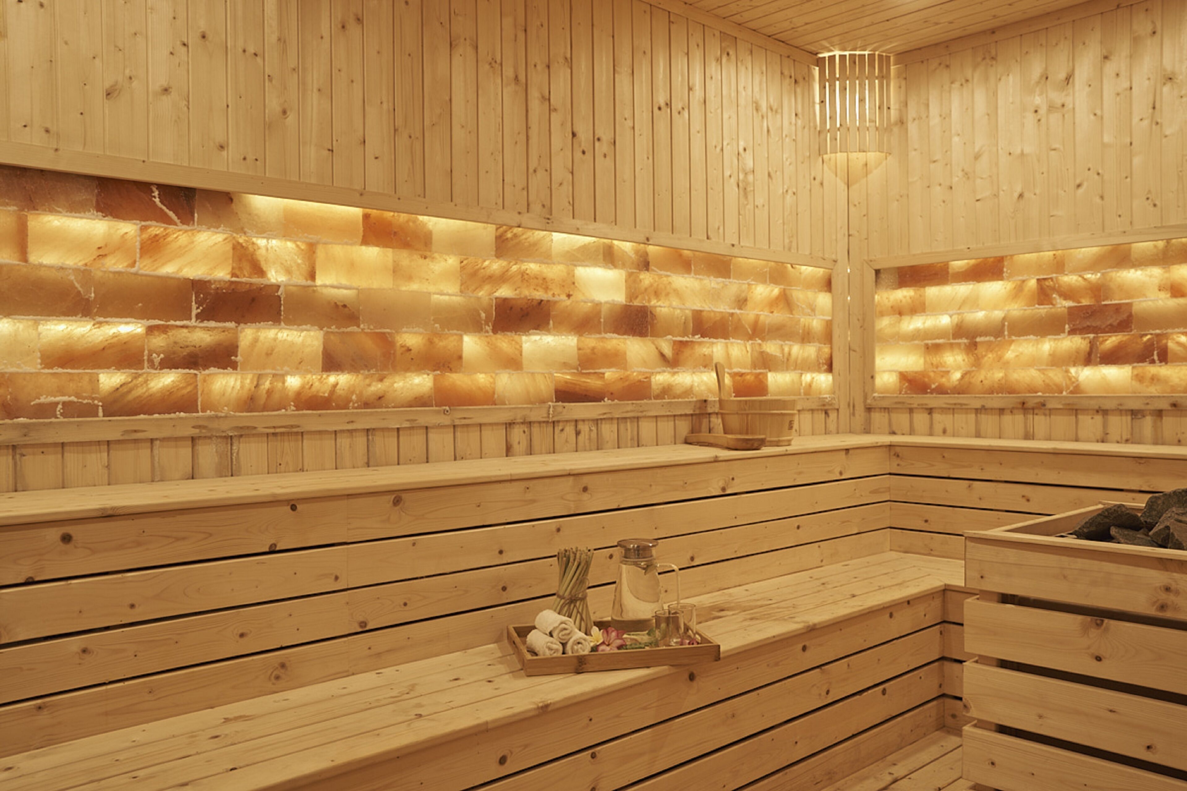 Un sauna en bois avec des bancs, un plateau contenant des serviettes et une bouteille.
