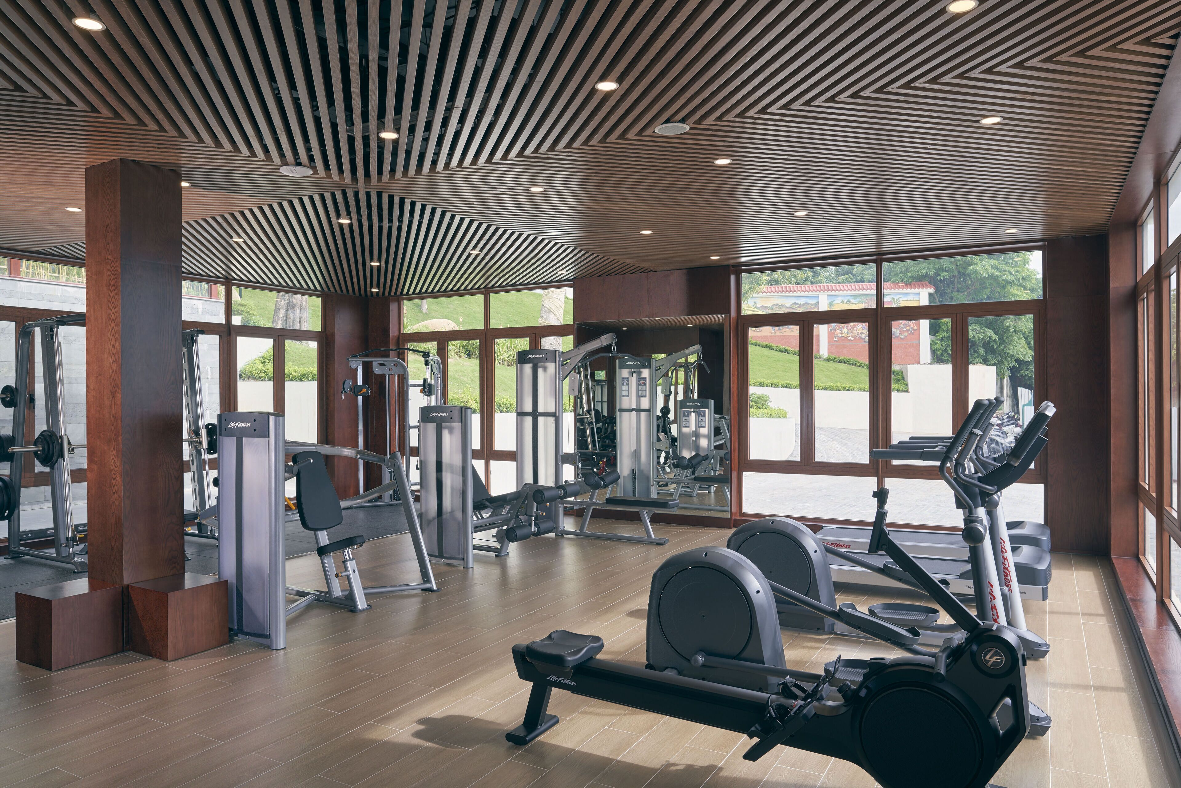 A gym with various exercise equipment, large windows, and a modern ceiling design.