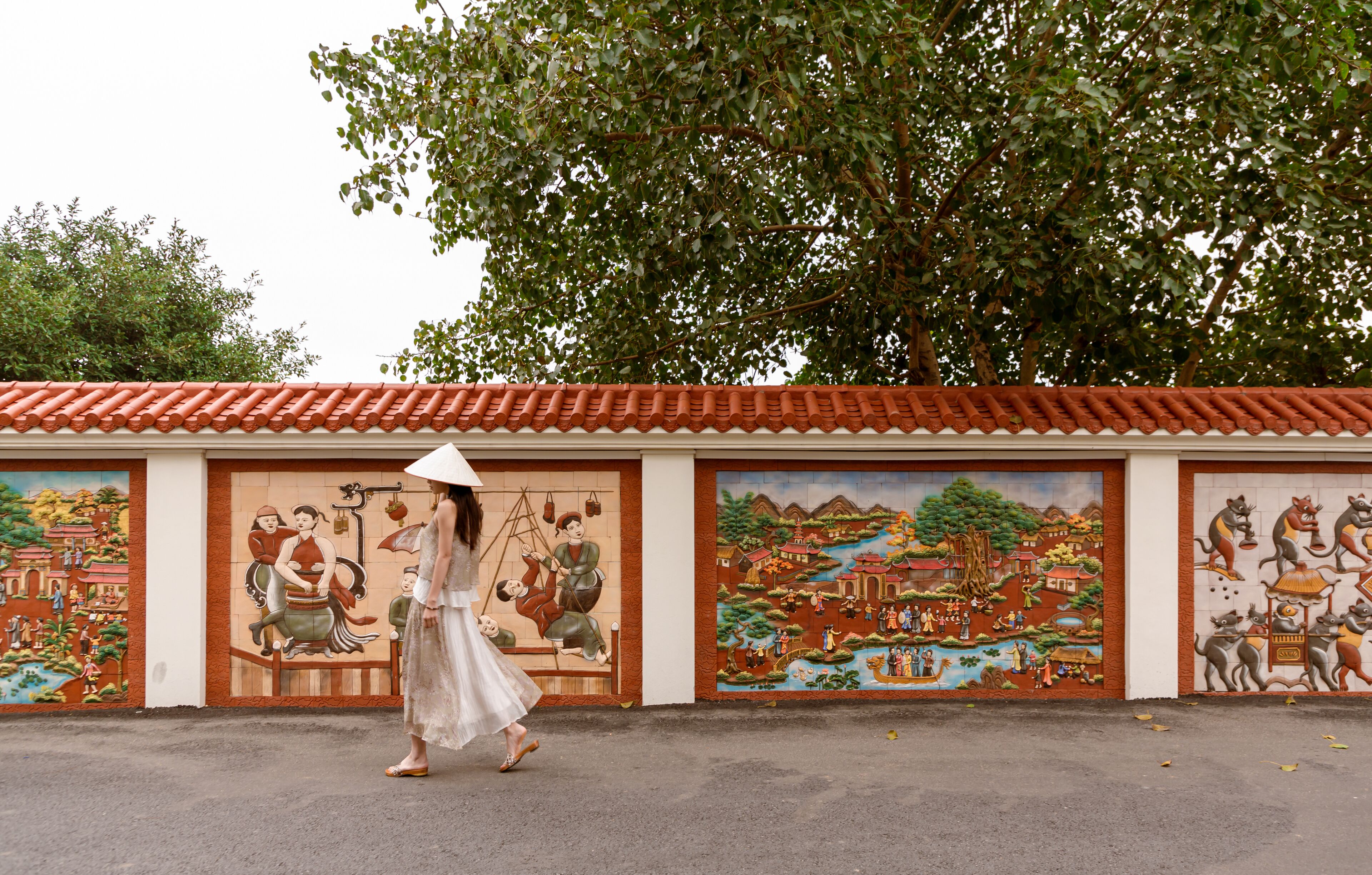 A woman in a white dress walking past a building with colorful murals depicting traditional scenes.
