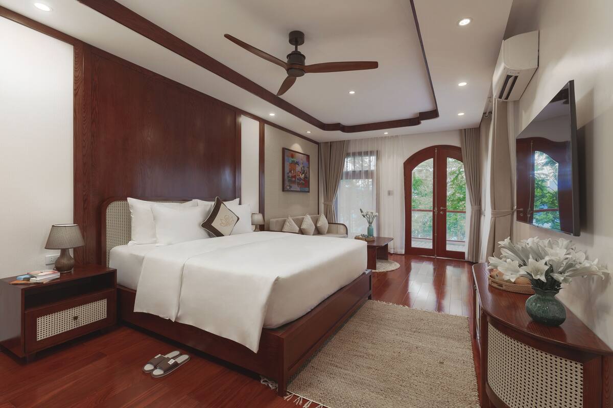 A spacious bedroom with a large bed, wooden headboard, a ceiling fan, a nightstand, a bedside table, and a mirror.