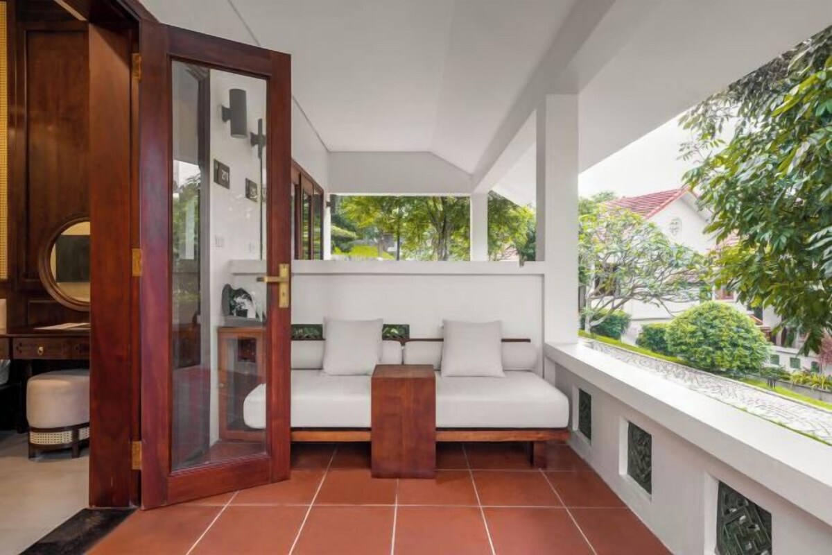 Un interior moderno con un sofá blanco, una mesita de madera y un ventanal de vidrio que da a un espacio exterior con vegetación.