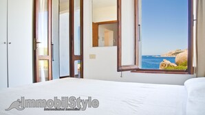Une chambre d’hôtel avec un lit, une armoire, un miroir et une fenêtre donnant sur la mer.