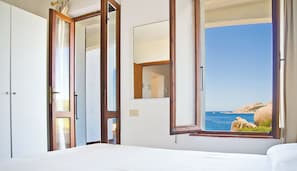 Ein Hotelzimmer mit Bett, Kleiderschrank, Spiegel und Fenster mit Meerblick.