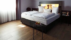 A hotel room with a large bed, a bedside table with a lamp, and a small stool with fruit. - Brauhotel & Gasthof GROSCH (Roedental)
