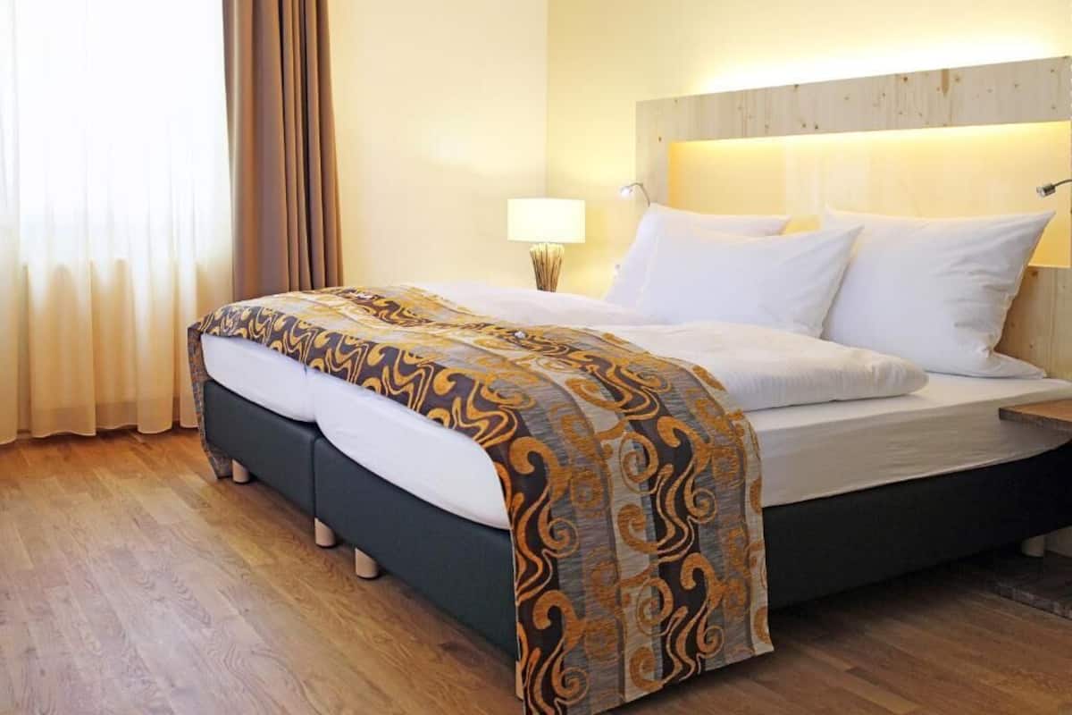 Een hotelkamer met een bed, houten vloeren, een hoofdbord en een nachtkastje met een lamp.