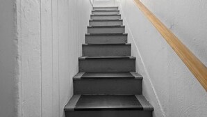 Una escalera estrecha con barandillas de madera y paredes blancas.