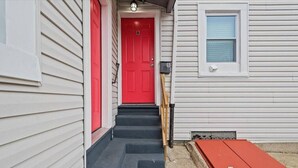 Una casa con una puerta roja, un conjunto de escaleras que conducen a la puerta principal y un pequeño objeto rojo en el suelo.