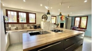 Une cuisine moderne dotée d’un îlot central, d’appareils électroménagers intégrés et de grandes fenêtres.