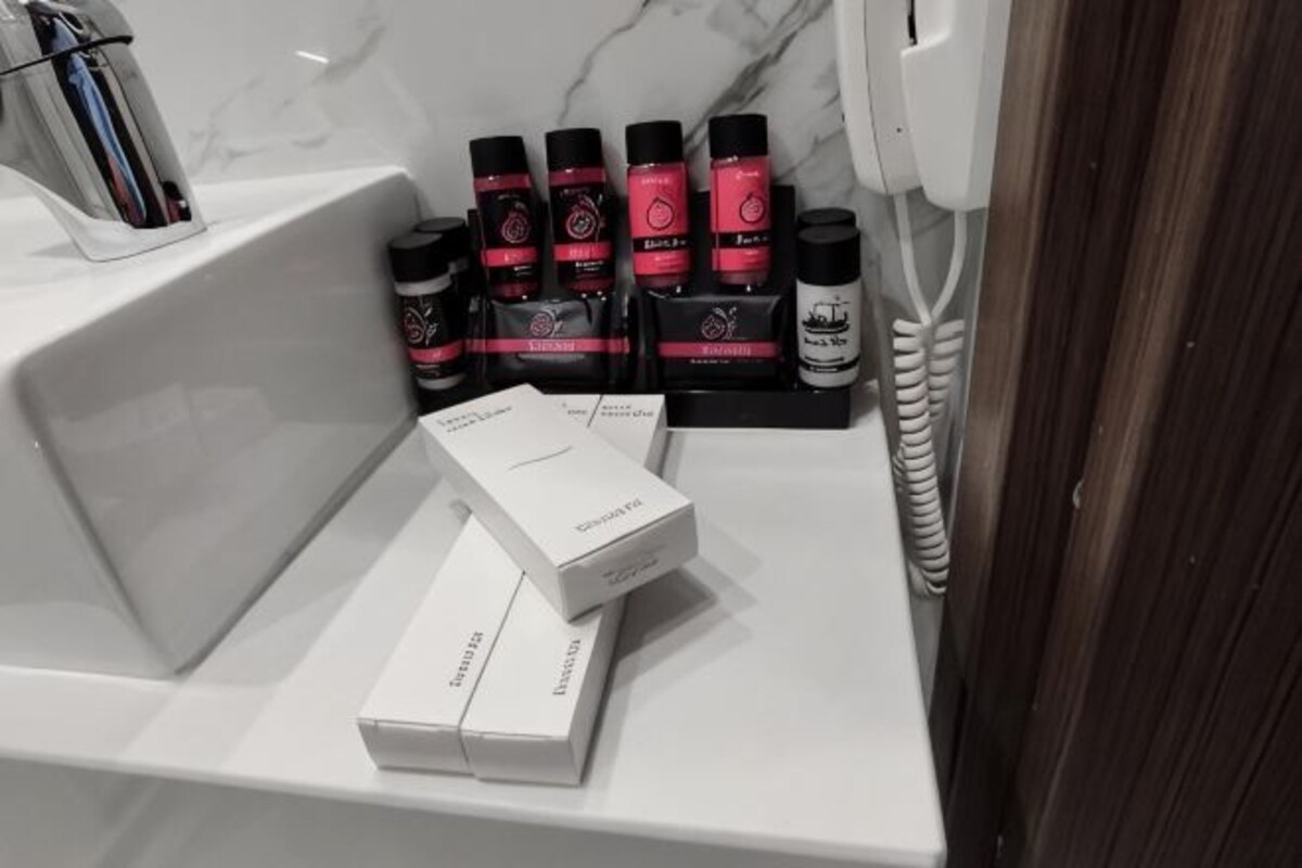 Ett badrum med ett vitt handfat, en spegel och ett set med hygienartiklar, inklusive flaskor och förpackningar.