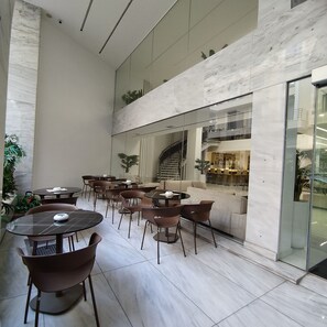 A spacious indoor area with multiple tables and chairs, a staircase, and a view of a restaurant or café in the background. - International Atene hotel (Athens)