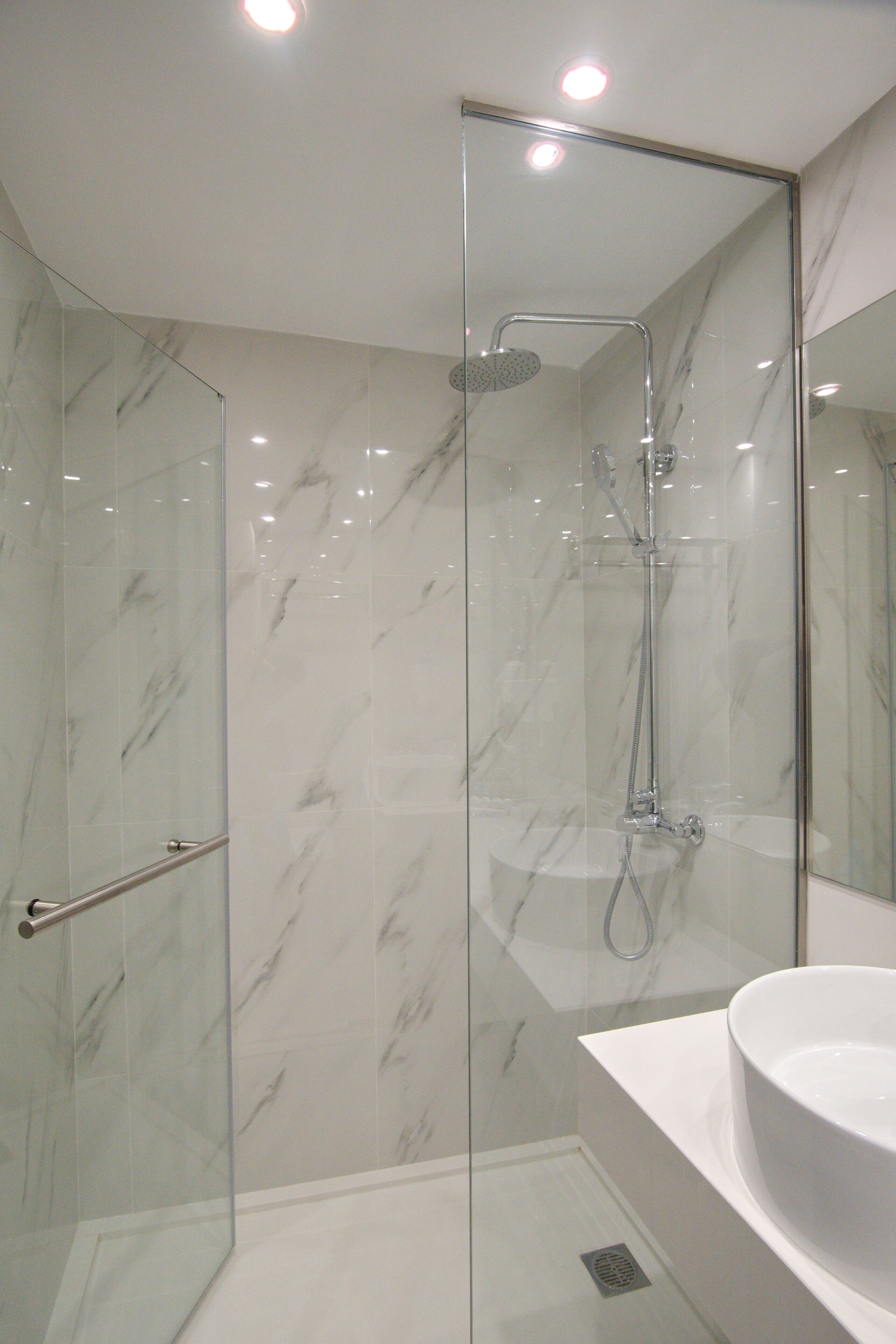 Un baño moderno con ducha de vidrio, un lavamanos blanco y paredes de mármol.