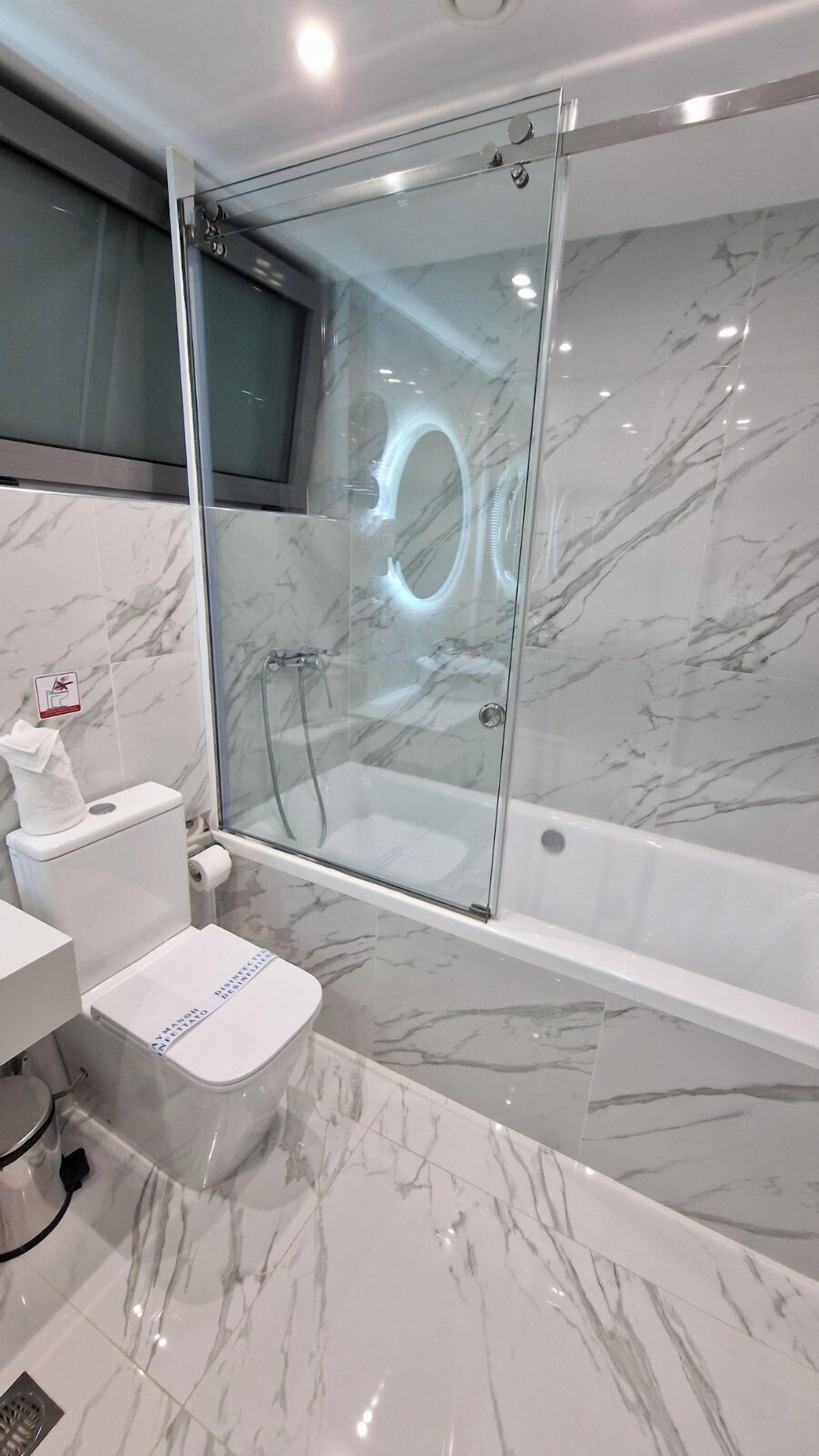 A modern bathroom with a glass-enclosed shower, a toilet, and a bathtub.