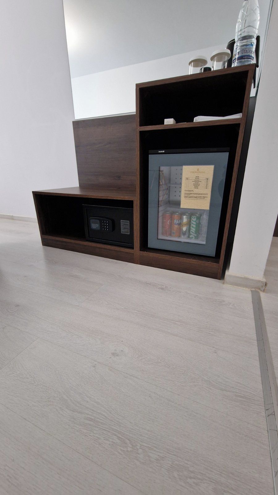 A corner cabinet with a built-in safe, a small shelf with a framed menu, and a water bottle on top.