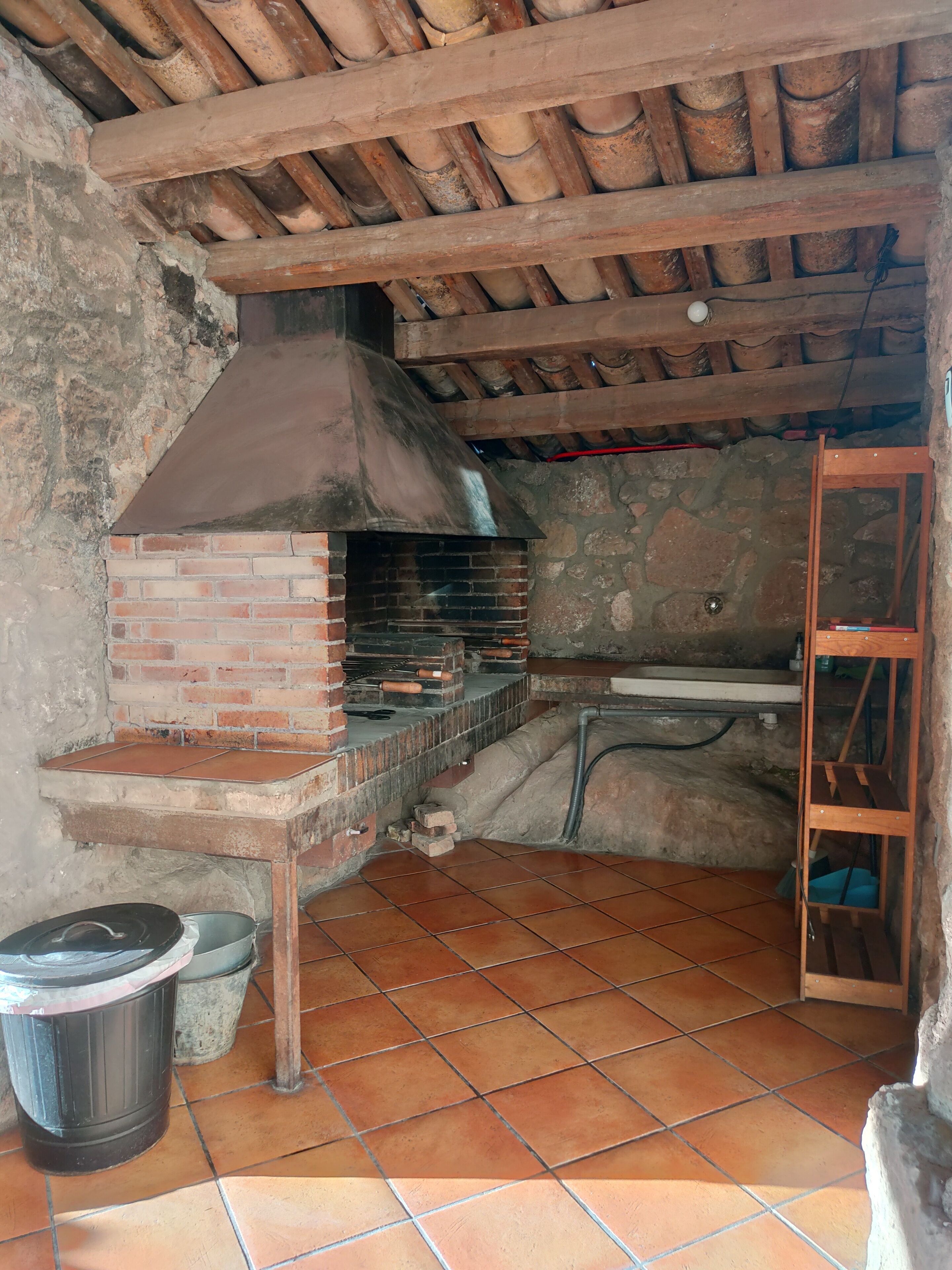 A rustic kitchen with a brick oven, stone walls, and a wooden ceiling.