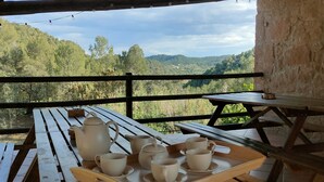 Una mesa de madera al aire libre con una bandeja de teteras y tazas, frente a un paisaje montañoso.