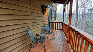 A wooden deck with two metal chairs and a table, a railing, and a view of trees. - The Fairy Woods Cabin in Banner Elk, NC, offers a cozy retreat for up to 8 guests. (Banner Elk)