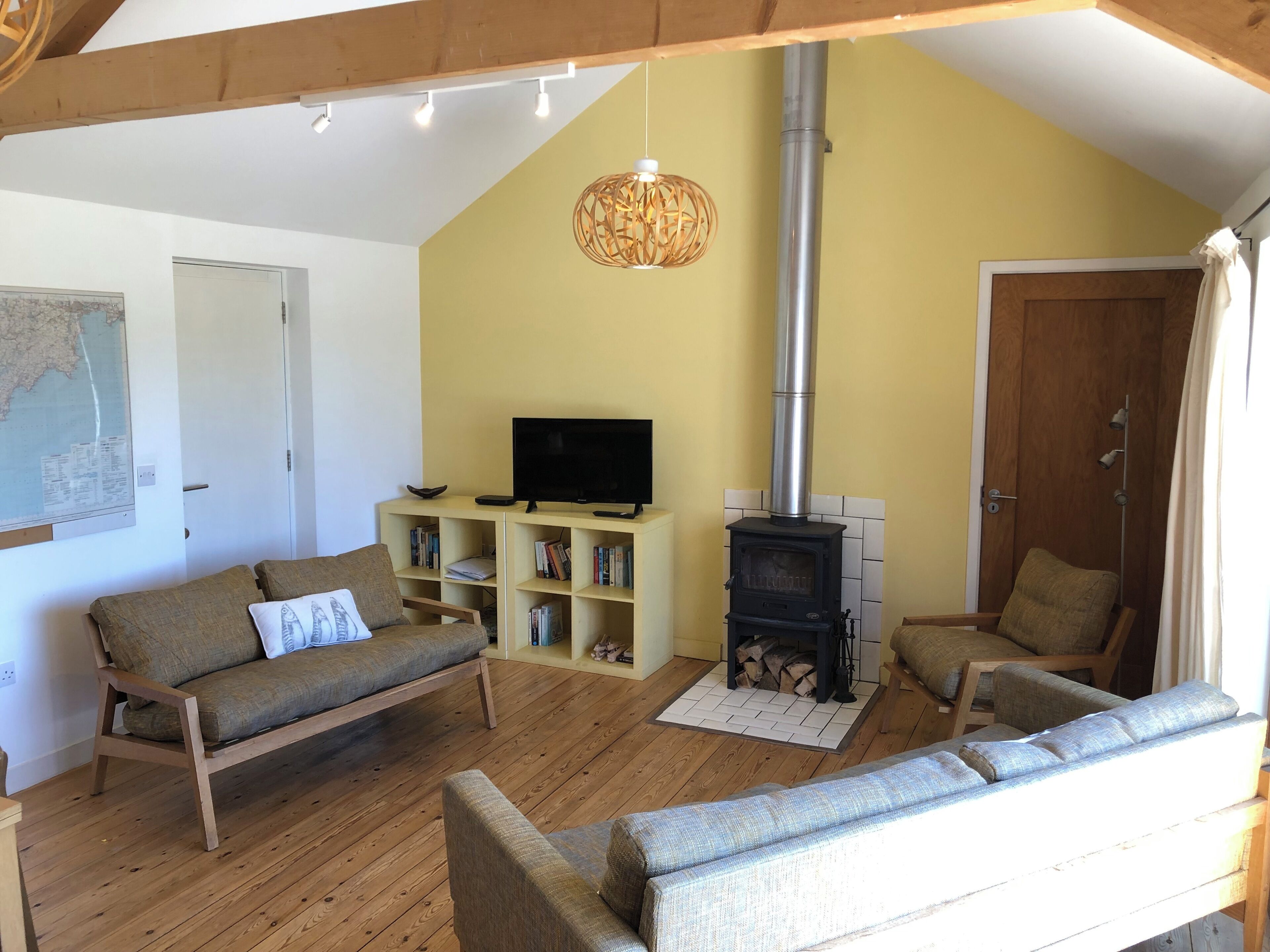 A cozy living room with a wooden floor, a sofa, a TV on a stand, a bookshelf, and a wood-burning stove.