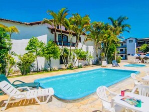 A swimming pool with lounge chairs, surrounded by palm trees and a white building with a tiled roof. - Portal Torres Hotel (Torres)