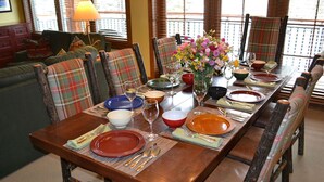 A dining table set with plates, bowls, and cutlery, surrounded by plaid chairs, with a sofa and a lamp in the background. - Ski-in Ski-out Luxurious 3 Bed 3 Bth + Free Ski Passes @ Teton Club (Jackson)