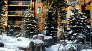 A snow-covered outdoor area with a stone wall, metal railings, and a building in the background. - Ski-in Ski-out Luxurious 3 Bed 3 Bth + Free Ski Passes @ Teton Club (Jackson)