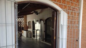 An interior corridor with a tiled floor, a brick wall, and a metal gate. - House with Pool in Itanhaém – Family and Pets (Itanhaém)