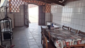 A spacious dining area with a long table and chairs, a tiled wall, and a ceiling fan. - House with Pool in Itanhaém – Family and Pets (Itanhaém)