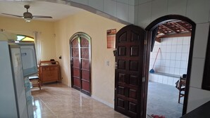 A hallway with a tiled floor, a ceiling fan, a refrigerator, a wooden cabinet, and a door with a metal mesh. - House with Pool in Itanhaém – Family and Pets (Itanhaém)