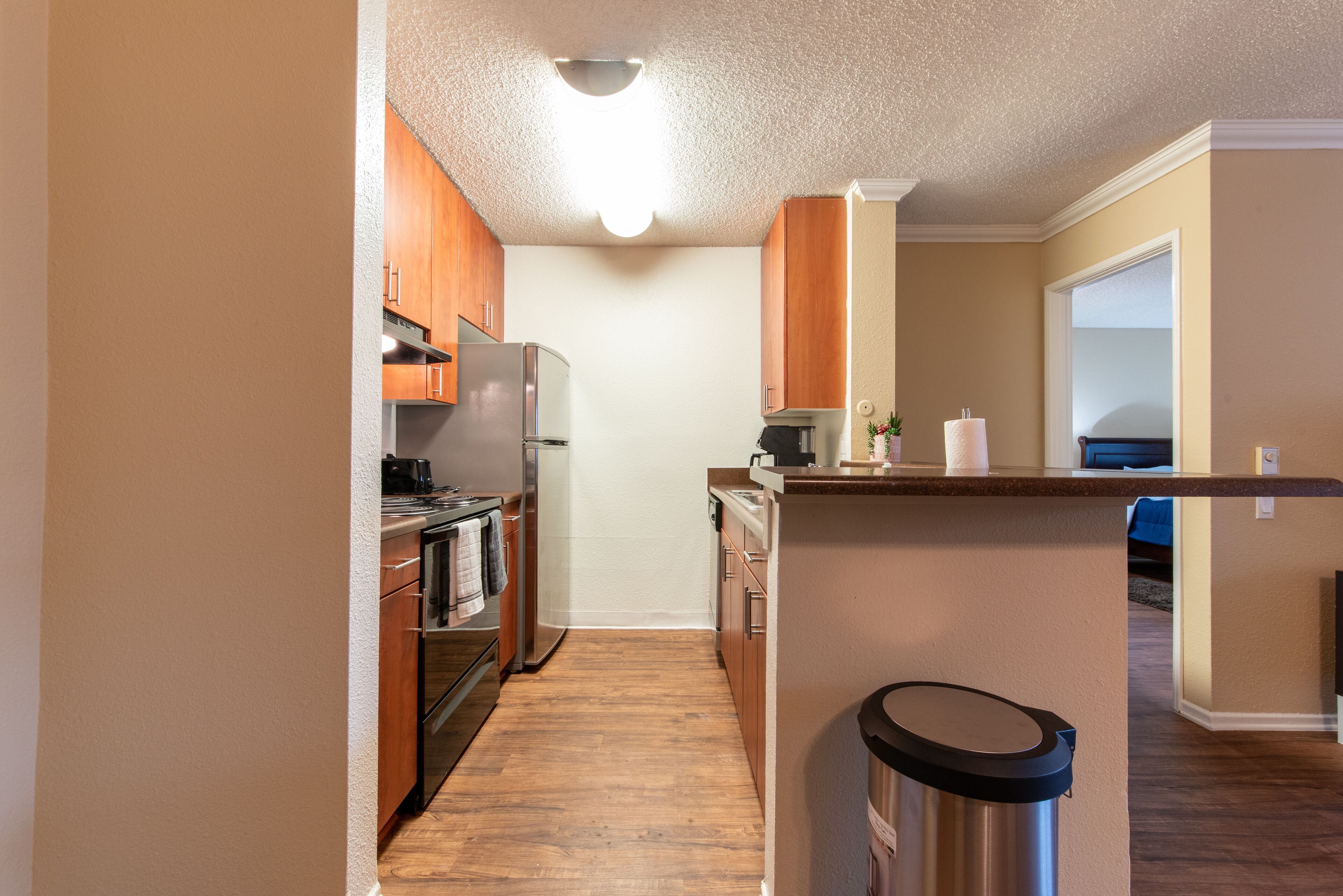 A kitchen with wooden cabinets, stainless steel appliances, and a trash can.